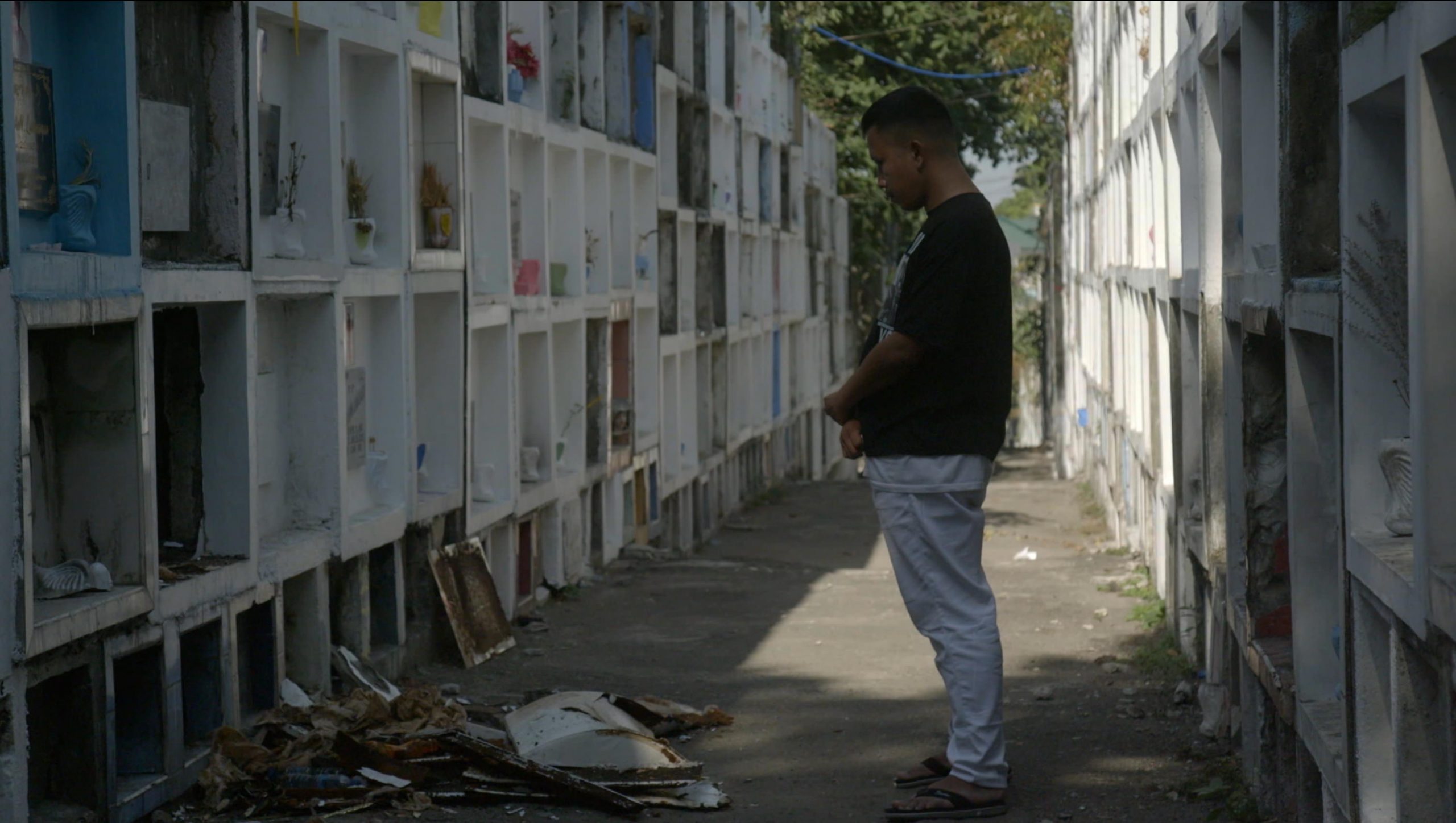Asiatischer Mann steht in einer Urnenreih auf dem Friedhof und betet